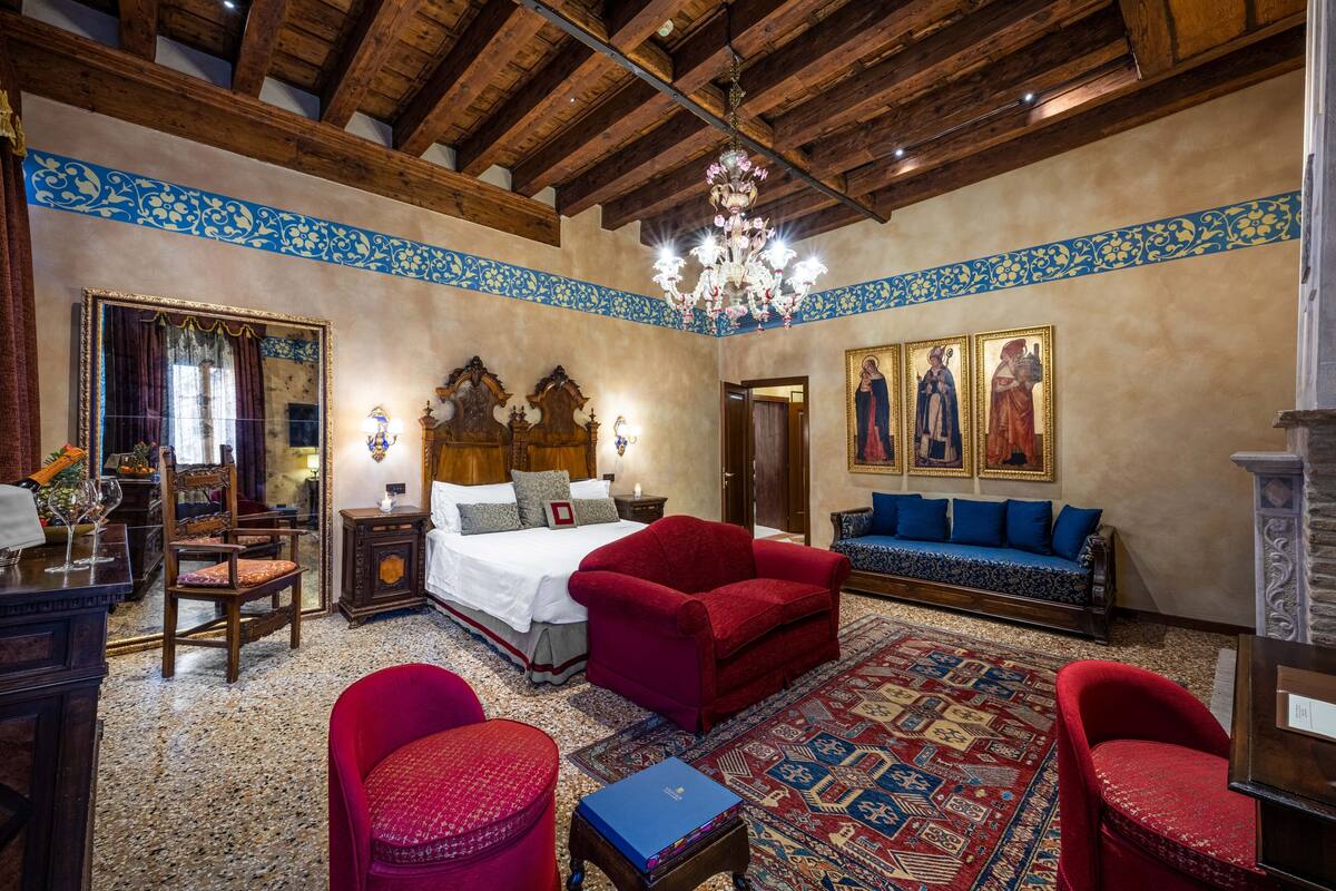 A traditional room with a wooden ceiling, a large bed, a red sofa, a patterned rug, and a chandelier.