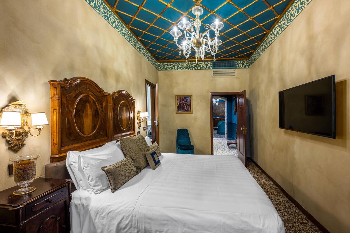 A hotel room with a large bed, a chandelier, a TV, and a wooden headboard.