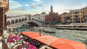 Un pont historique enjambant une rivière, avec des gondoles et un bateau, le tout entouré de bâtiments traditionnels dotés de balcons.