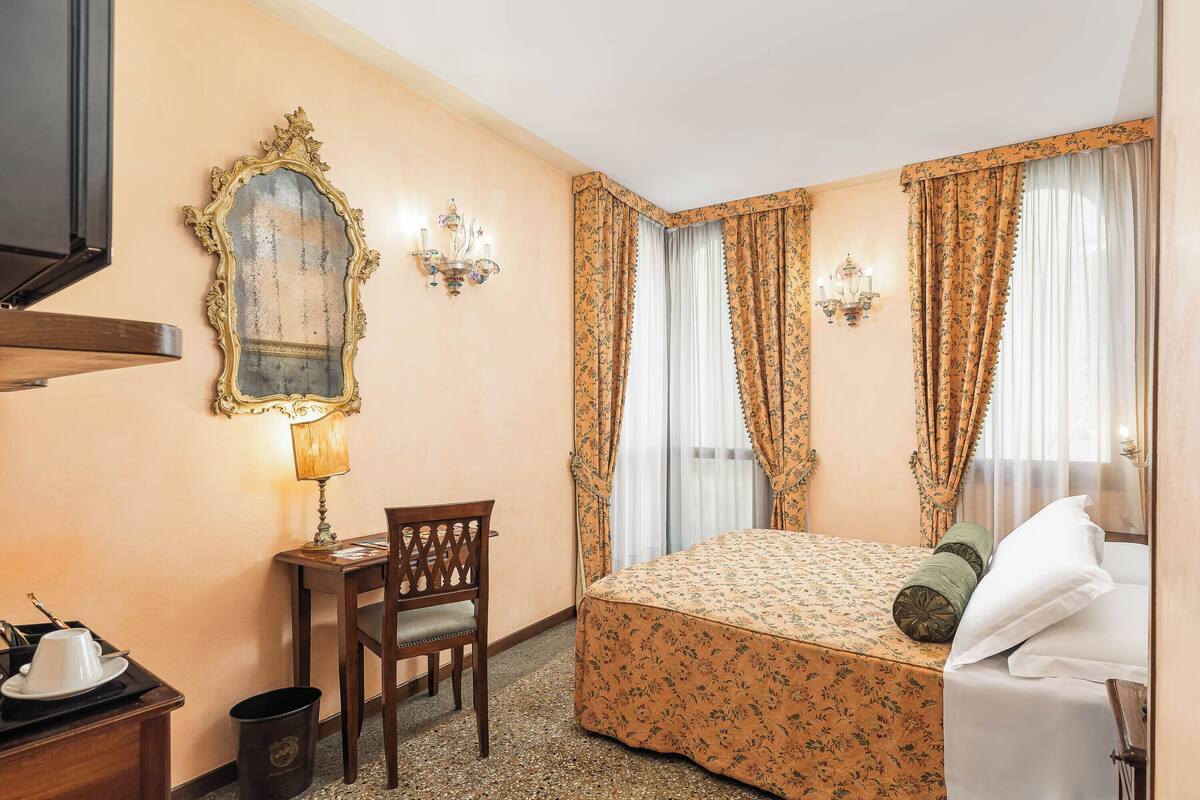 Una habitación de hotel con una cama, un escritorio con una silla, un espejo y cortinas.