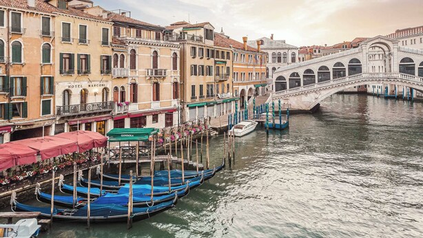 Un canal bordé de bateaux amarrés, un pont et des bâtiments dotés de balcons et d’auvents.