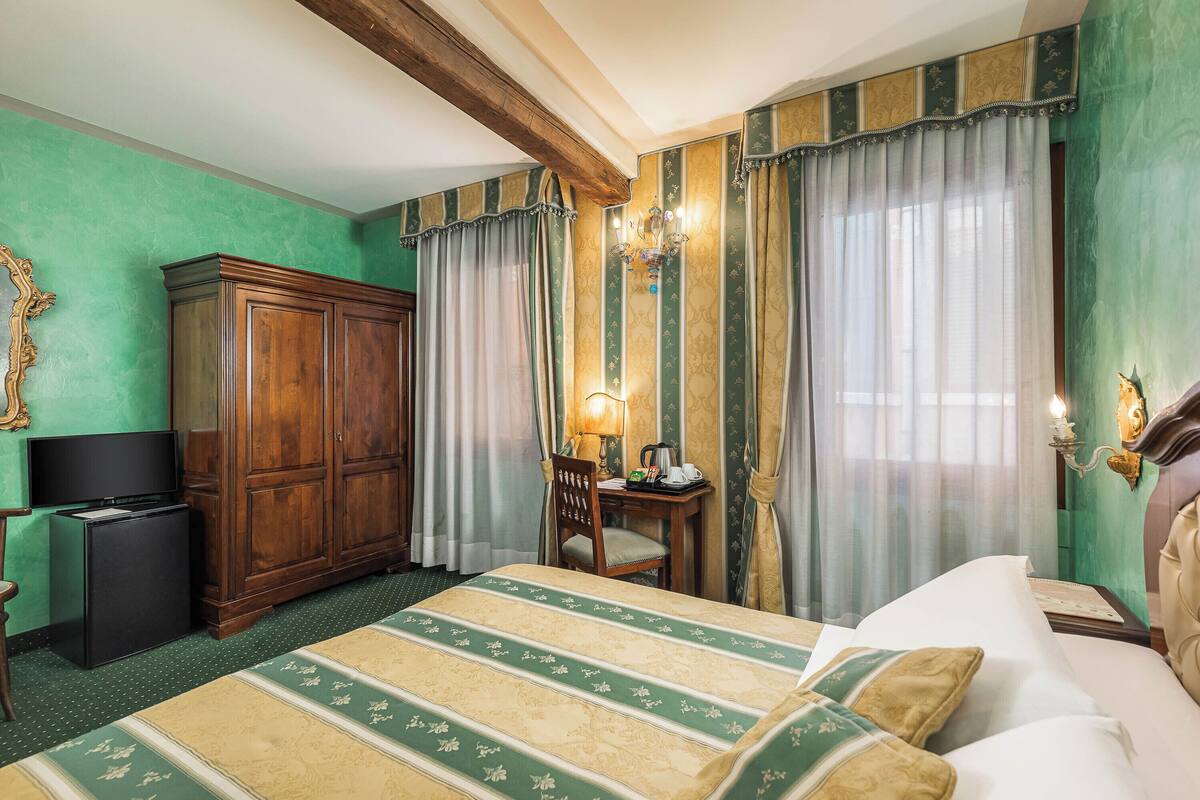 Una habitación de hotel con una cama grande, un armario de madera, un escritorio con lámpara y una televisión.