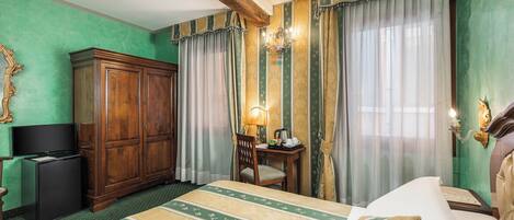 A hotel room with a large bed, a wooden wardrobe, a desk with a lamp, and a television.