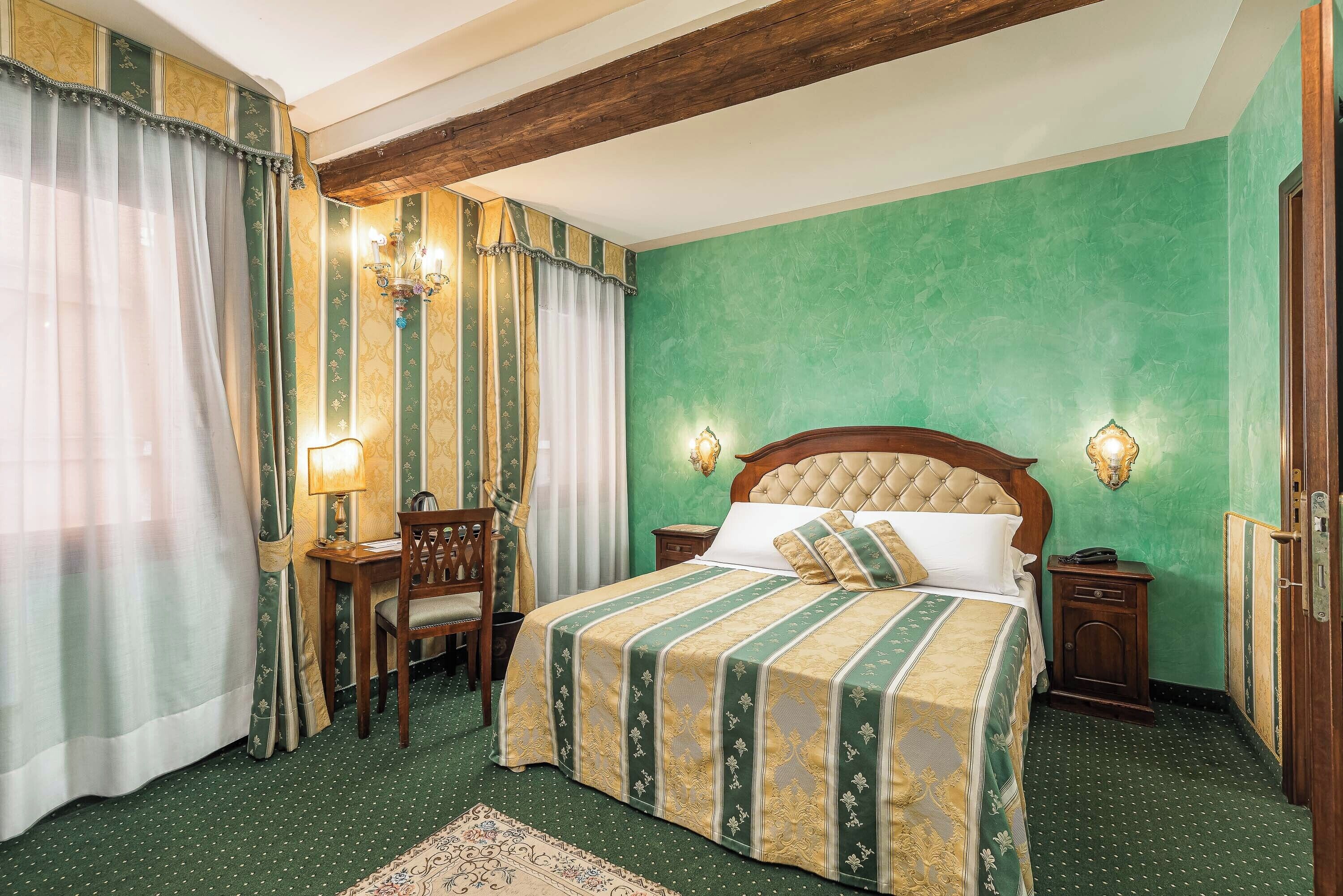 A hotel room with a large bed, a wooden headboard, two bedside tables with lamps, a chair, and a green carpet.