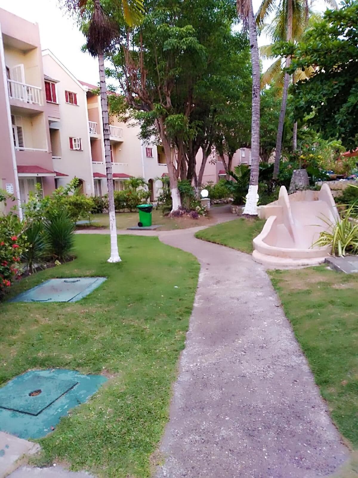 Un chemin menant à un bâtiment doté de nombreux balcons, entouré d’une végétation luxuriante et de palmiers.