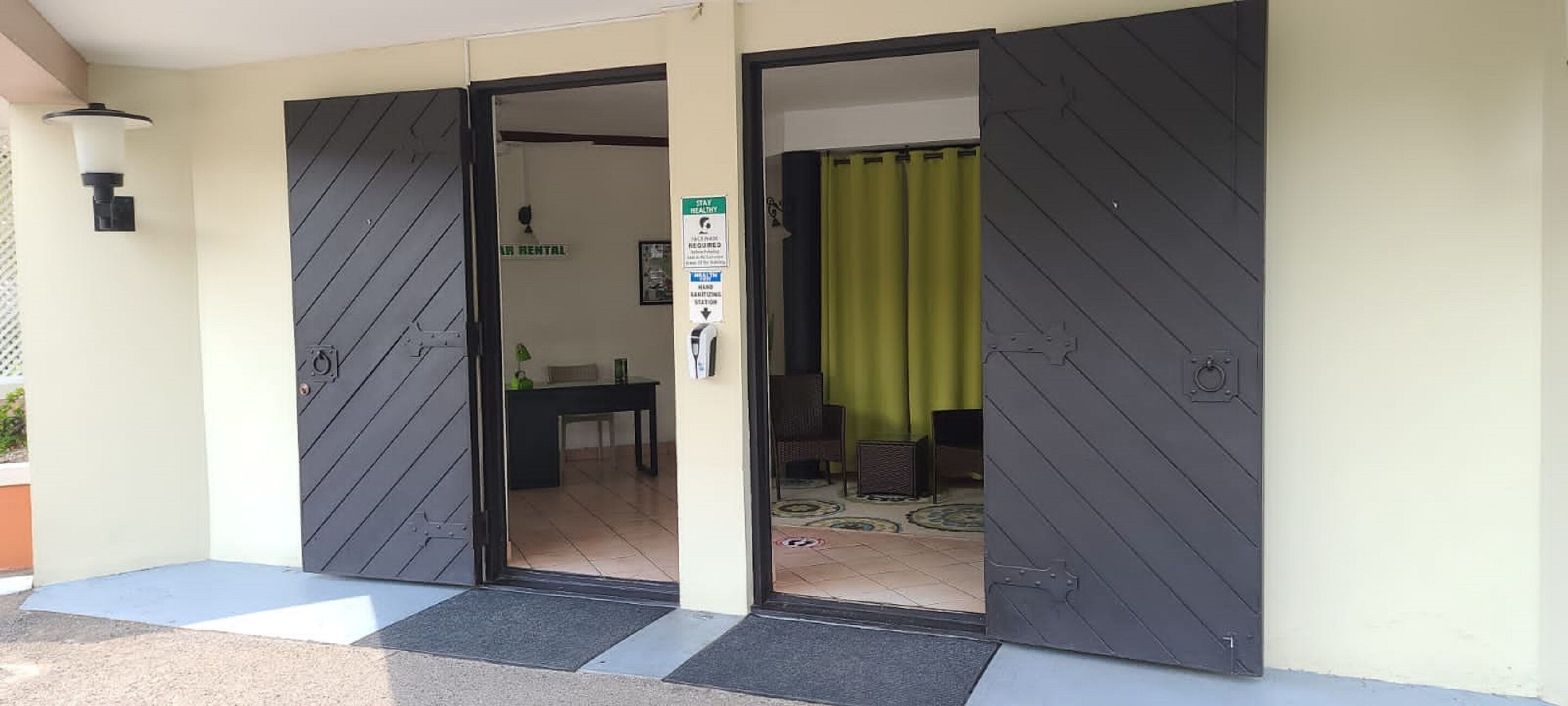 A hotel entrance with a closed door, a sign indicating a hand sanitizer station, and a green curtain partially visible.