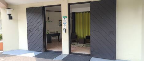 A hotel entrance with a closed door, a sign indicating a hand sanitizer station, and a green curtain partially visible.