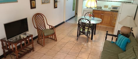 Una sala de estar con televisor, una silla de madera, una mesa de vidrio con sillas y un sofá.