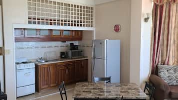 A compact kitchen with wooden cabinets, a refrigerator, a microwave, and a stove.