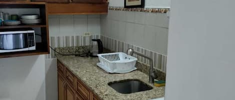 Una cocina compacta con armarios de madera, microondas, fregadero y estufa.
