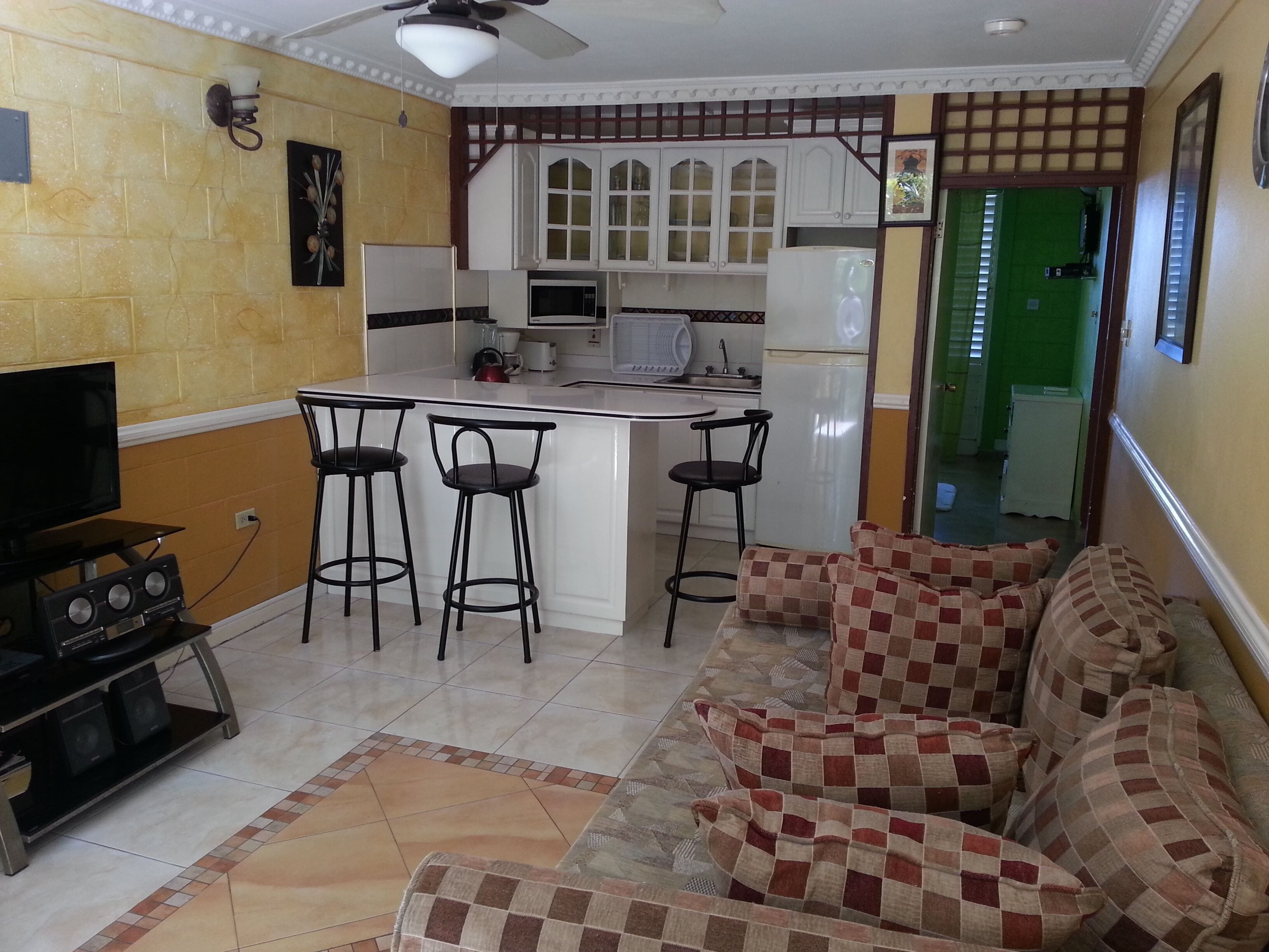 Un espacio habitable compacto con cocina, taburetes de bar, sofá y televisor.