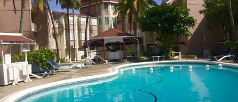 A swimming pool with lounge chairs, a covered seating area, and palm trees.