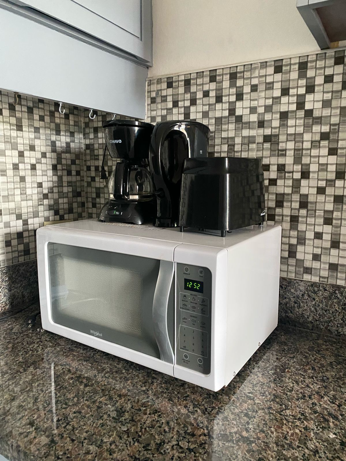 Een keuken met een witte magnetron, een zwarte koffiezetapparaat en een betegelde spatwand.
