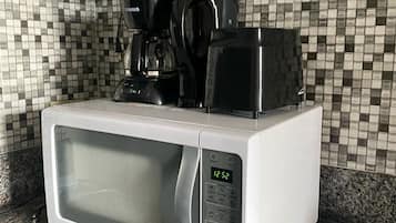 A kitchen with a white microwave, a black coffee maker, and a tiled backsplash.