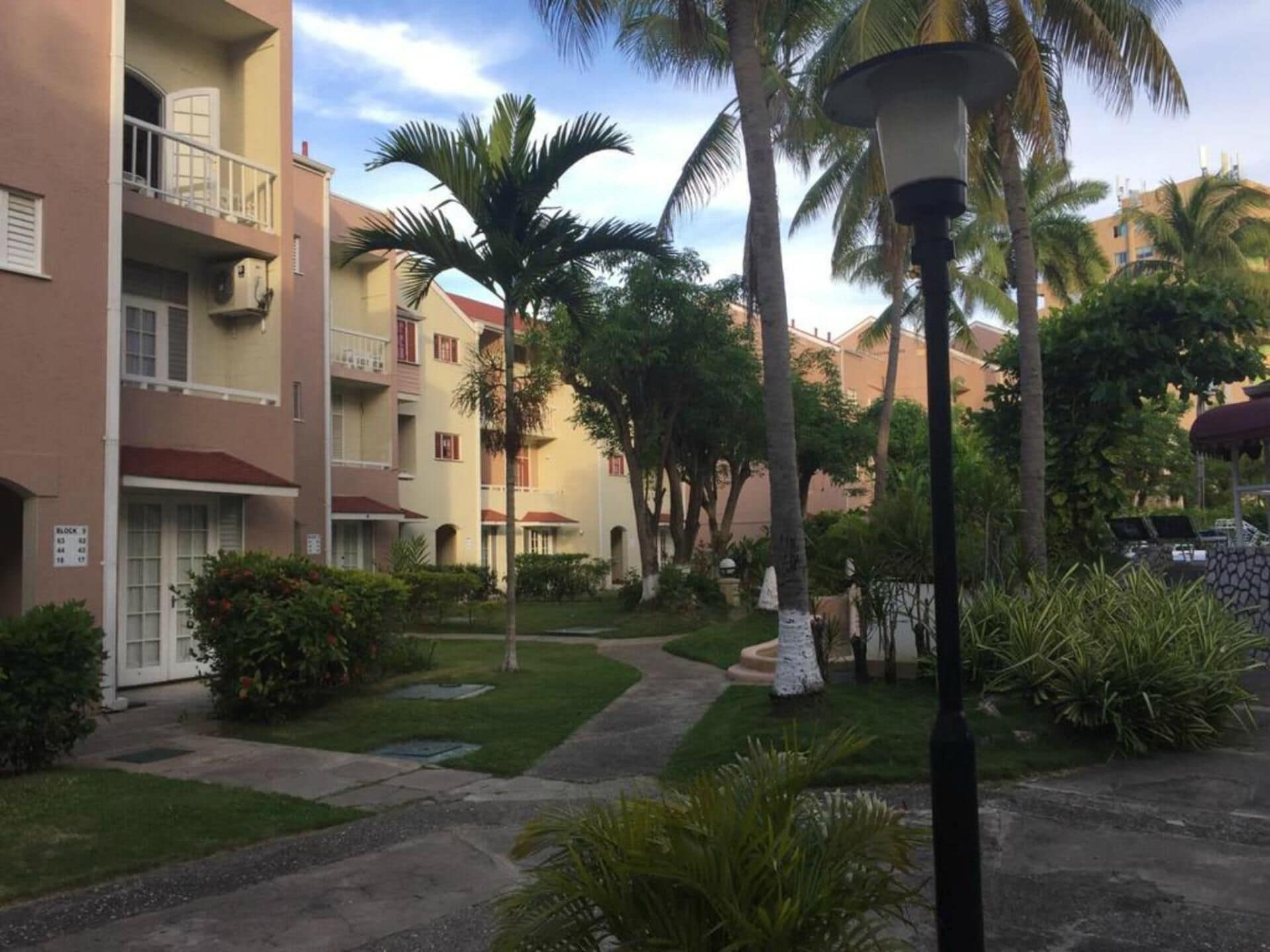 A courtyard with a pathway, palm trees, and a building with balconies.