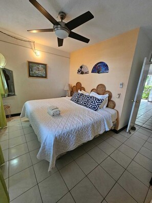 A hotel room with a bed, ceiling fan, wall art, and a window. - Fisherman's Point Resort (Ocho Rios)
