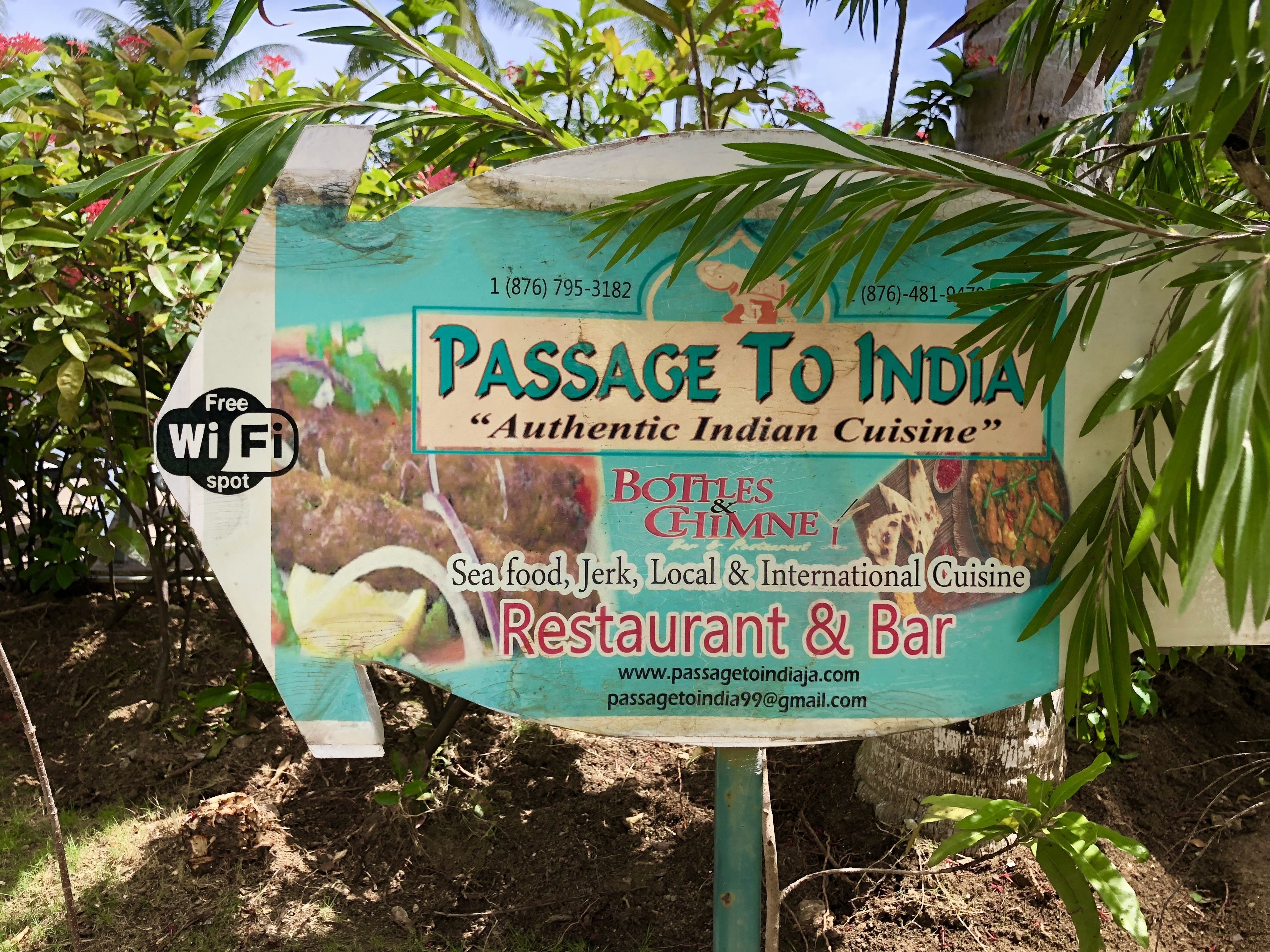 Passage To India -ravintolan ja -baarin kyltti, jossa mainitaan, että se tarjoaa aitoa intialaista ruokaa, sekä yhteystiedot ja verkkosivuston osoite.