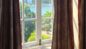A room with a large window, curtains, and a patterned cushion.
