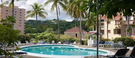 A pool area with lounge chairs, palm trees, and a building in the background.