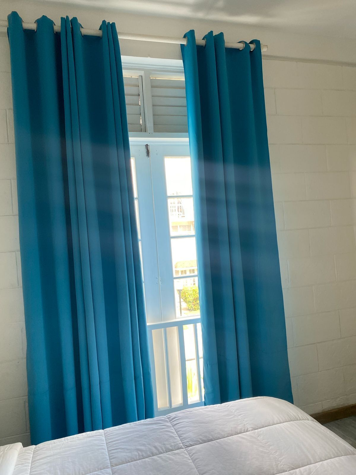 Quarto com uma cama, cortinas brancas e janela com vista para edifícios.