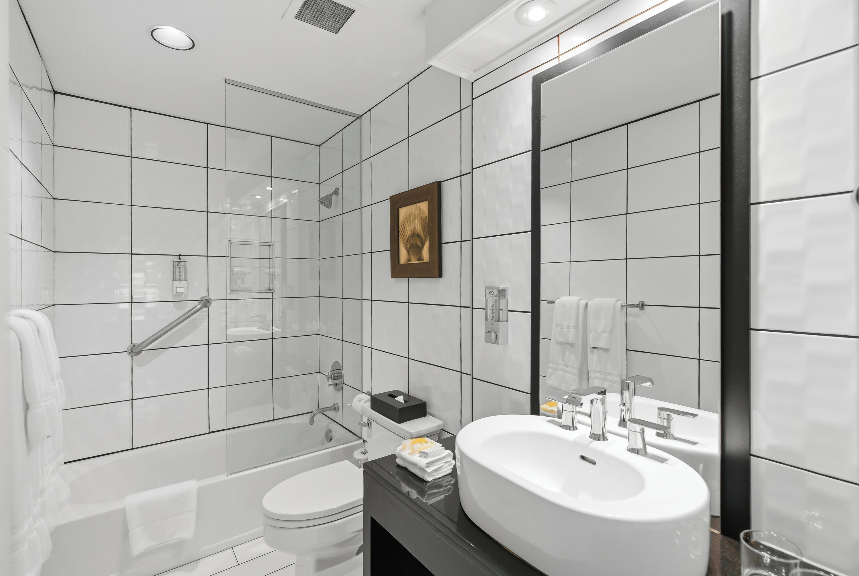 A modern bathroom with white tiles, a large mirror, a bathtub, a toilet, and a sink.