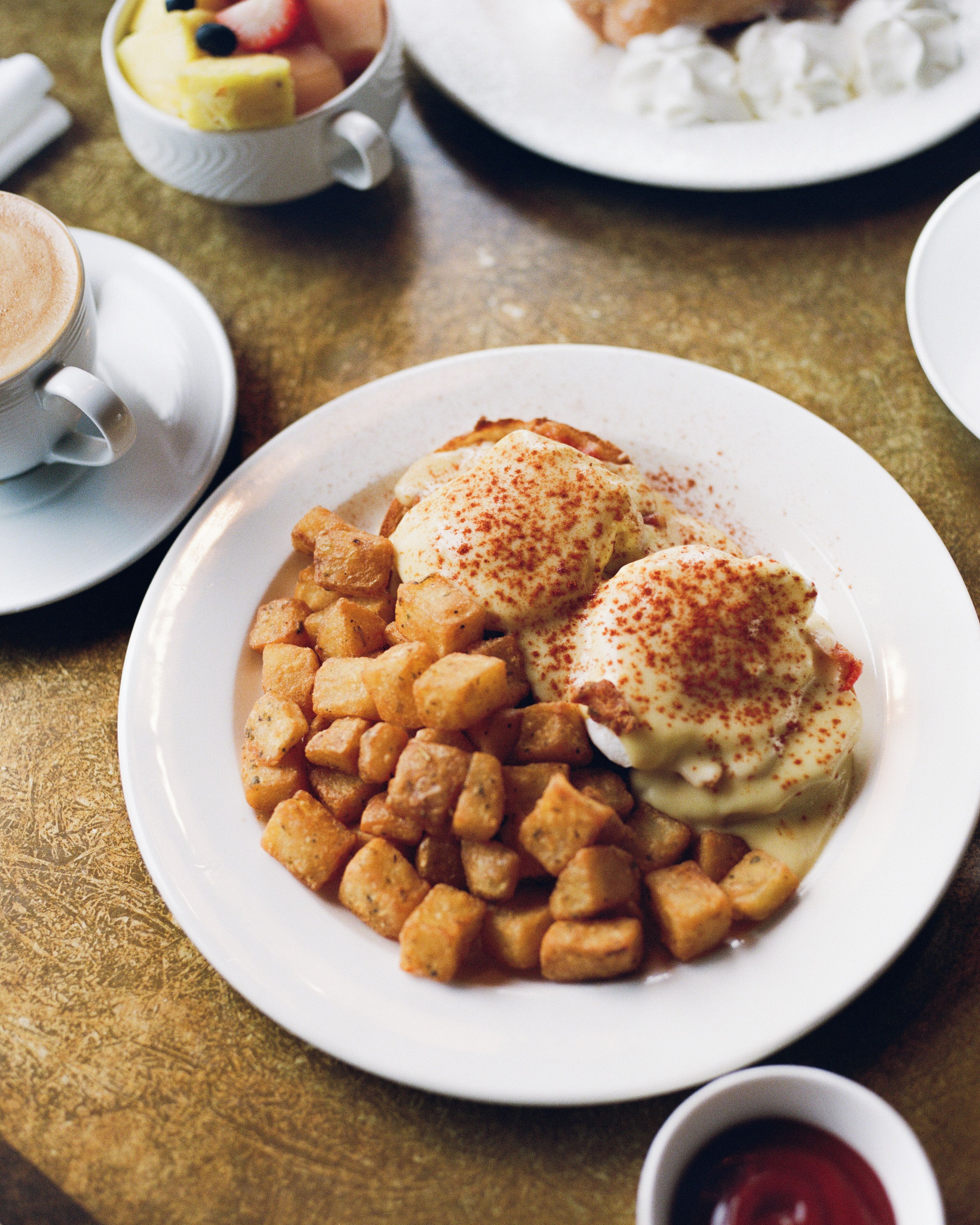 A dining table with plates of food, including a dish with poached eggs and potatoes, and a cup of coffee.