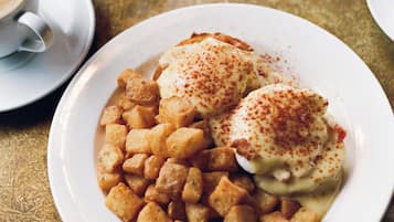 A dining table with plates of food, including a dish with poached eggs and potatoes, and a cup of coffee.