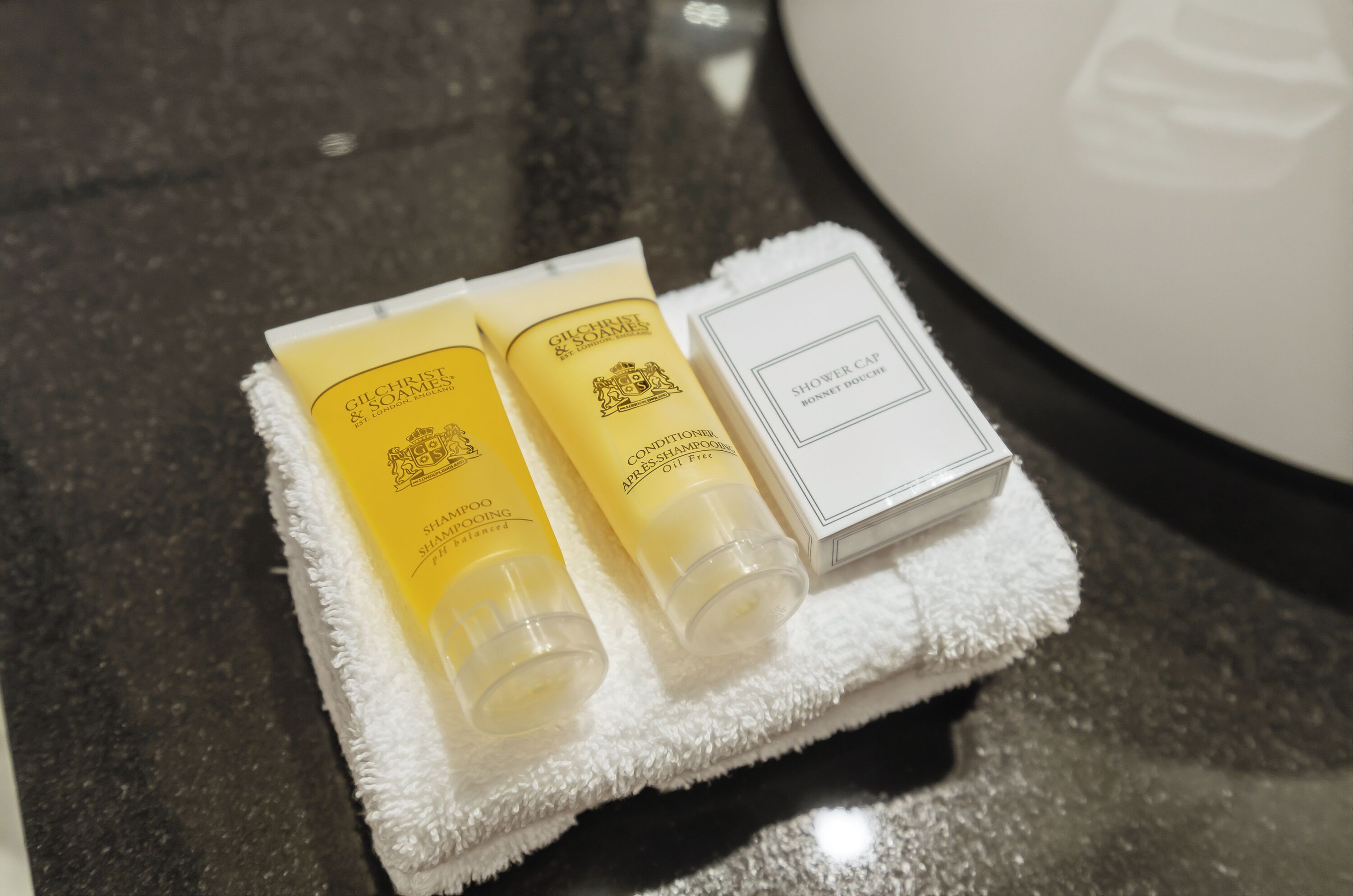 A set of toiletries on a white towel, including a shower cap and two bottles of conditioner.