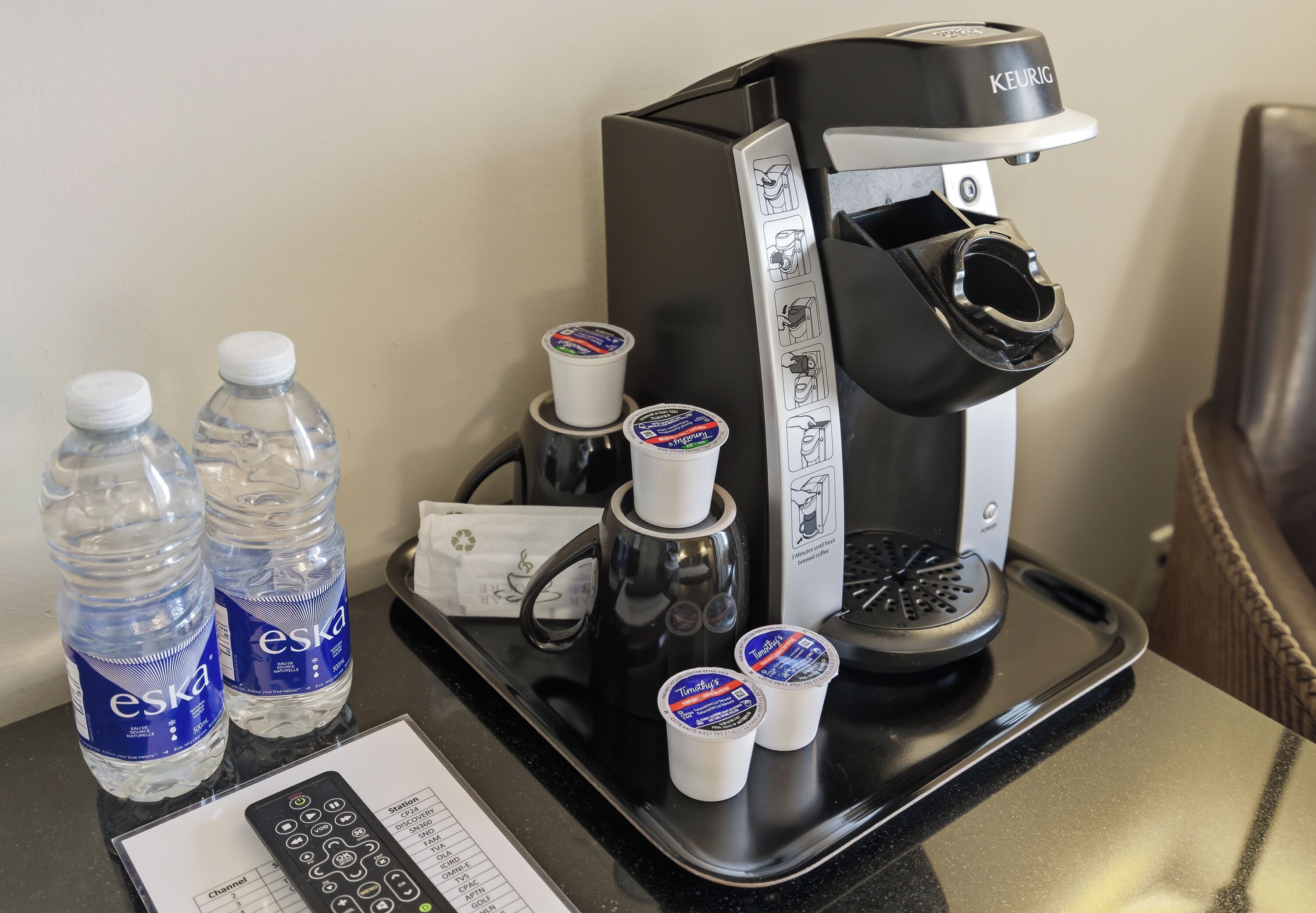 Uma cafeteira, duas garrafas de água Eska e duas canecas de café Tim Hortons em um suporte.