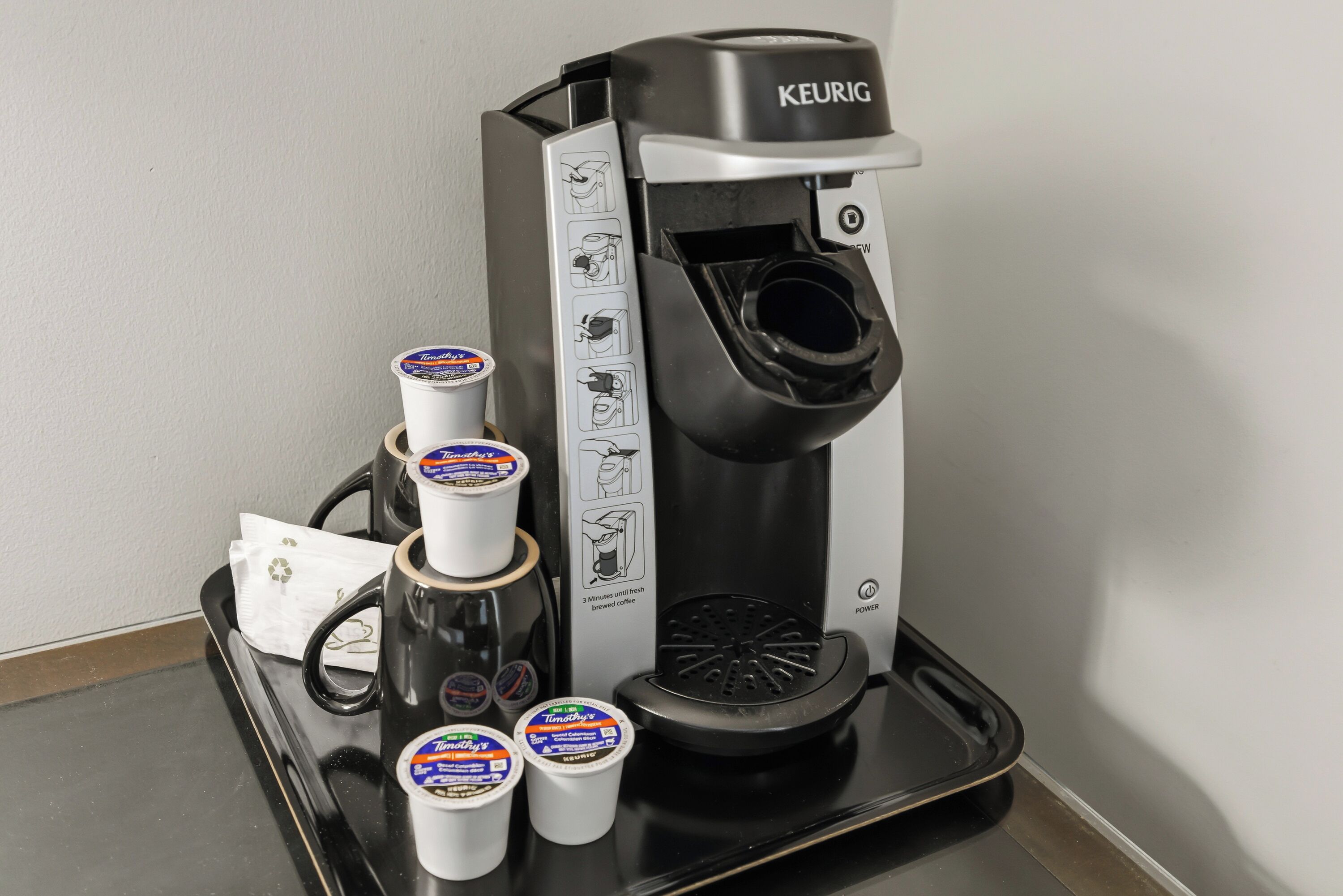 A Keurig coffee machine with instructions, a tray, and three Tim Hortons cups.