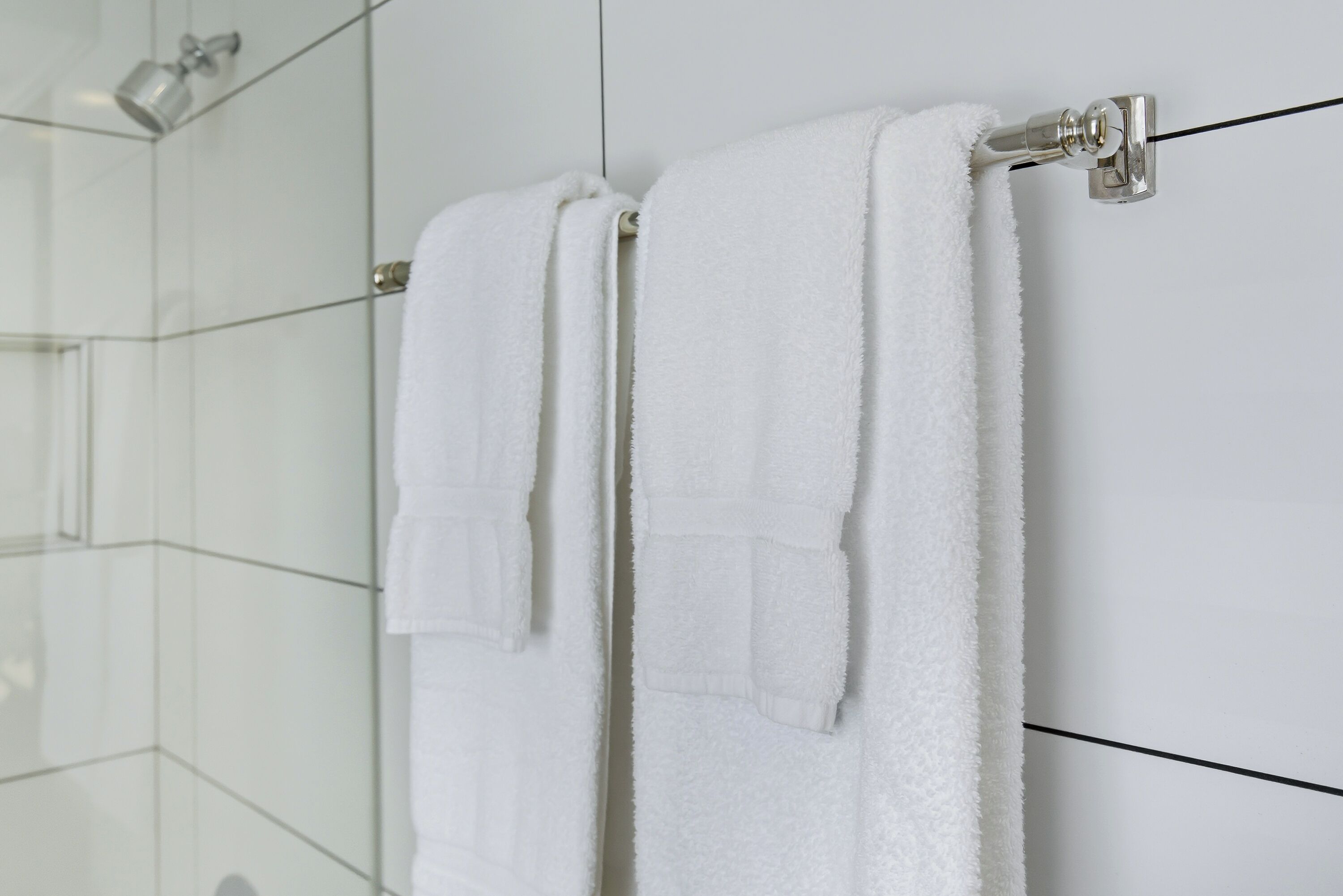 A white towel hanging on a metal towel rack in a bathroom with tiled walls.