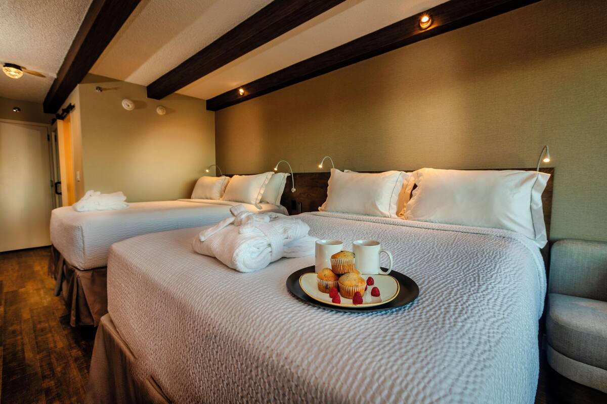 Habitación de hotel con dos camas, una bandeja con muffins y café, y toallas dobladas cuidadosamente.