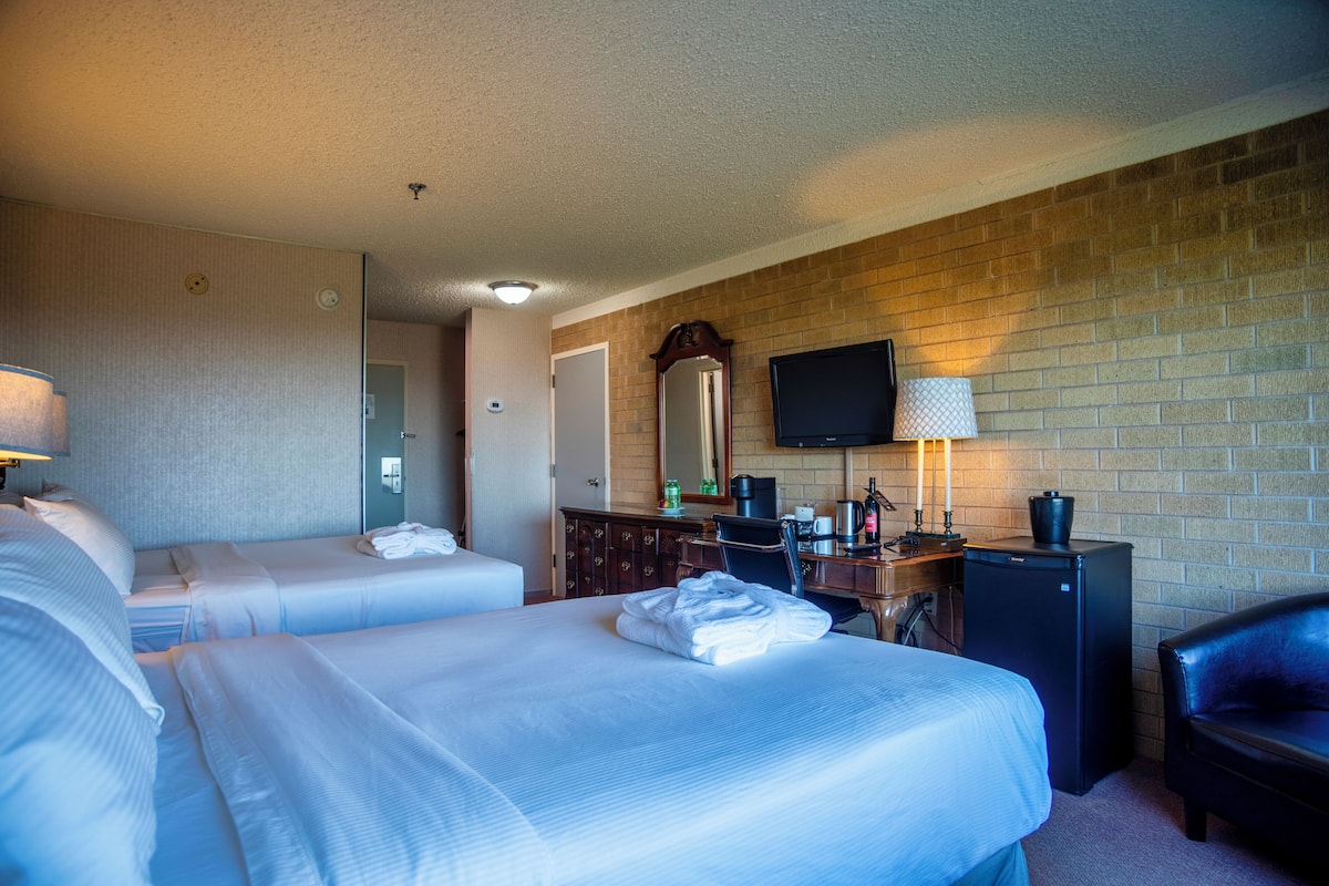 Habitación de hotel con dos camas, un escritorio con computadora, televisión y pared de ladrillo.