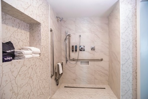 A walk-in shower with a handrail, a towel rack, and a shelf with folded towels.