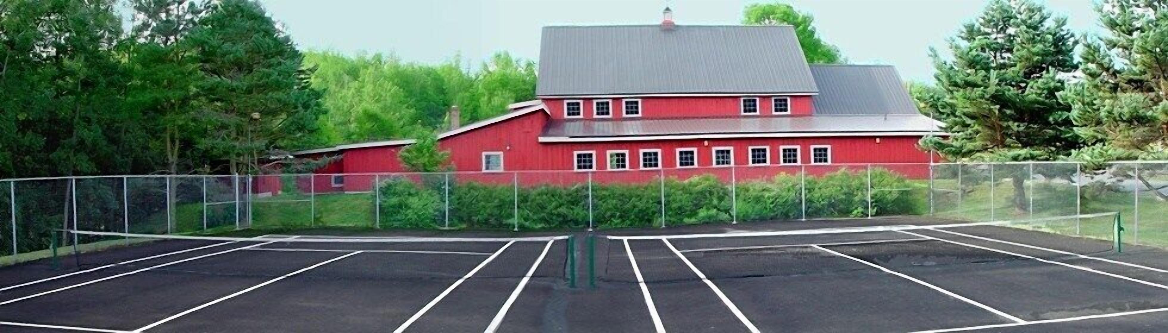 A red building with a grey roof, surrounded by green trees and bushes.
