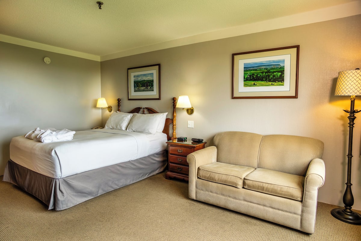 Una habitación de hotel con una cama, una silla, dos lámparas fijadas a la pared y dos cuadros enmarcados.