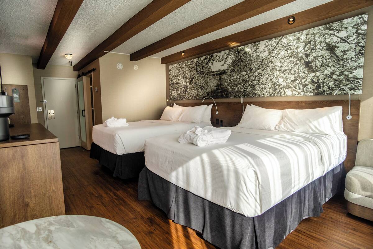 Habitación de hotel con dos camas, vigas de madera en el techo, un gran mural floral en la pared y un escritorio con teléfono.