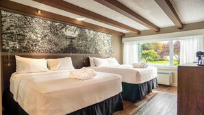 A hotel room with two beds, a large window with a view of the garden, and a wooden ceiling.