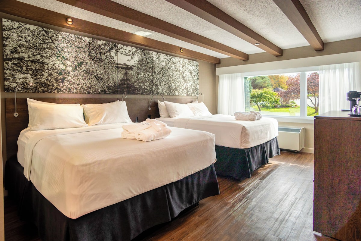 Habitación de hotel con dos camas, un ventanal grande con vistas al jardín y techo de madera.