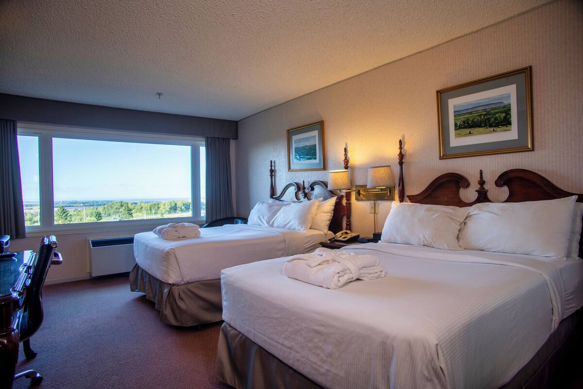 Habitación de hotel con dos camas, un escritorio y vistas al exterior.
