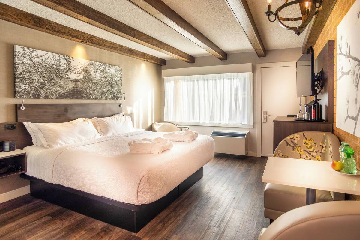 Una habitación de hotel moderna con una cama grande, una mesa de comedor y un ventanal con cortinas.