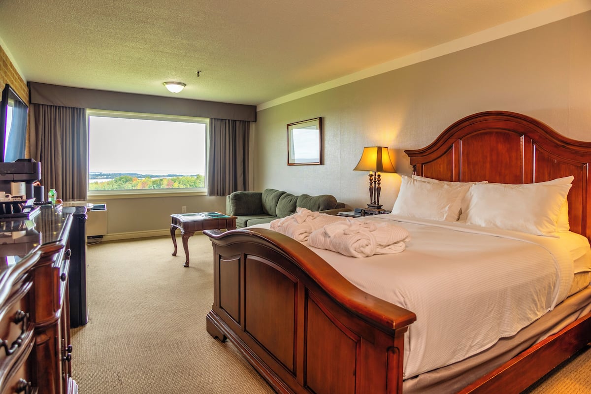 Habitación de hotel con una cama grande, un escritorio, una silla, una lámpara y vistas al exterior.