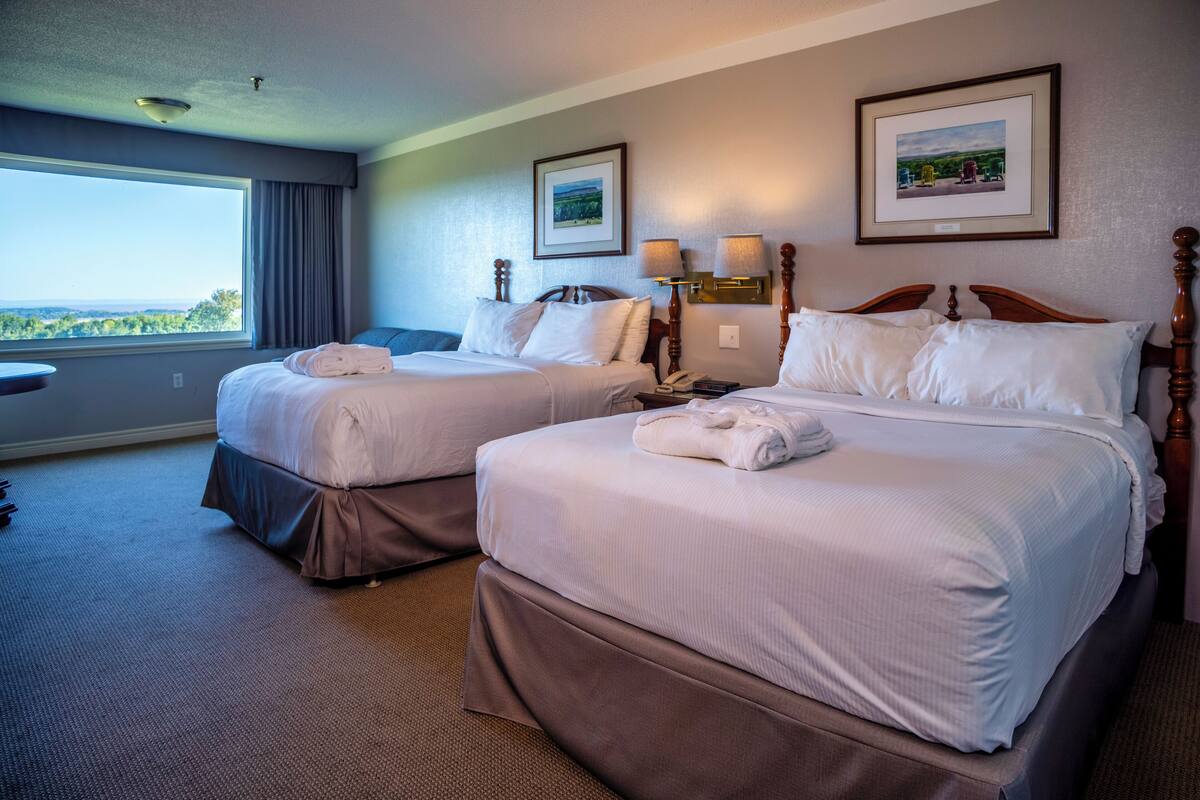 Habitación de hotel con dos camas, un ventanal grande y vistas al exterior.