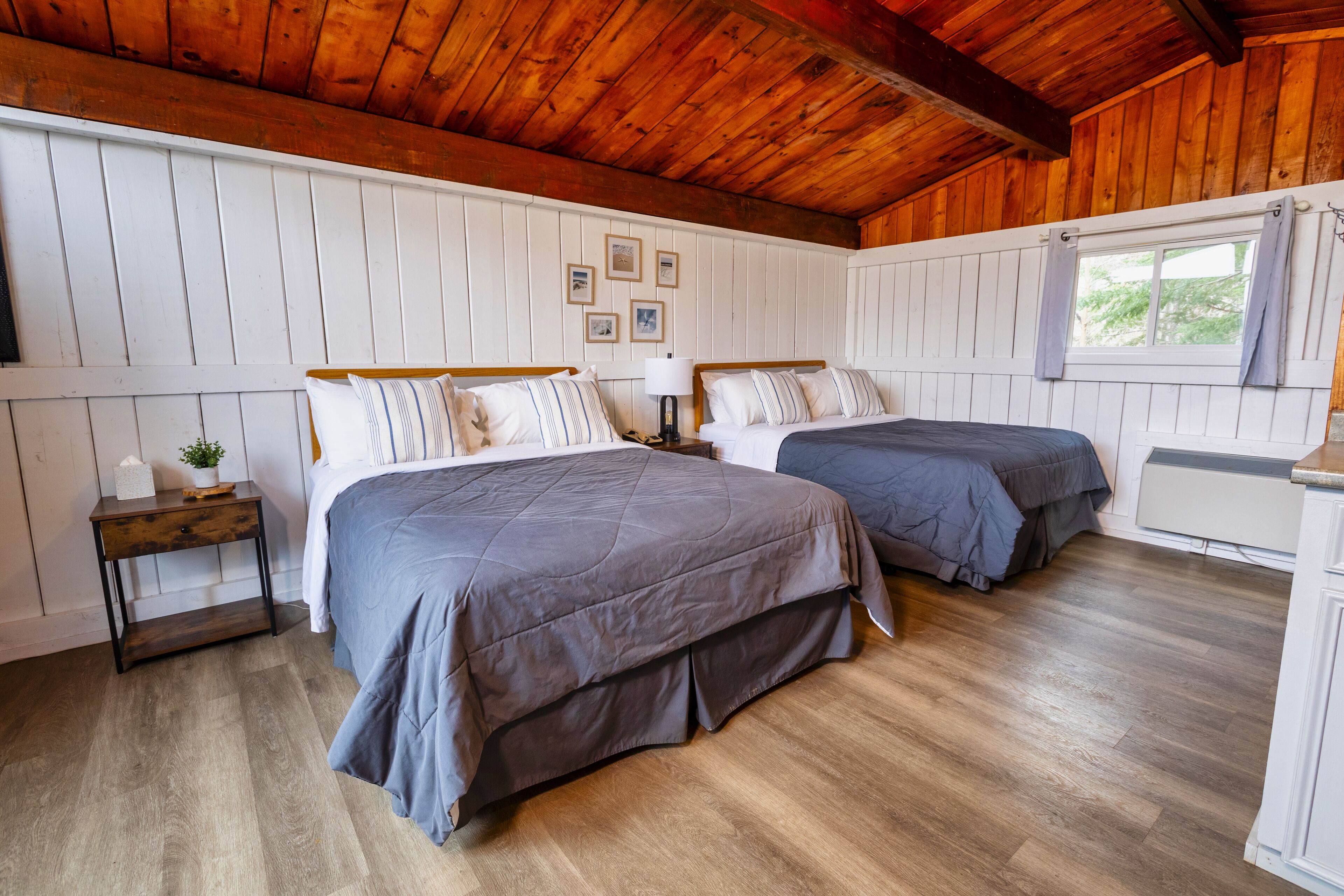 A room with two beds, wooden flooring, white walls, and a wooden ceiling.