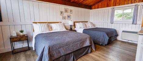 A room with two beds, wooden flooring, white walls, and a wooden ceiling.