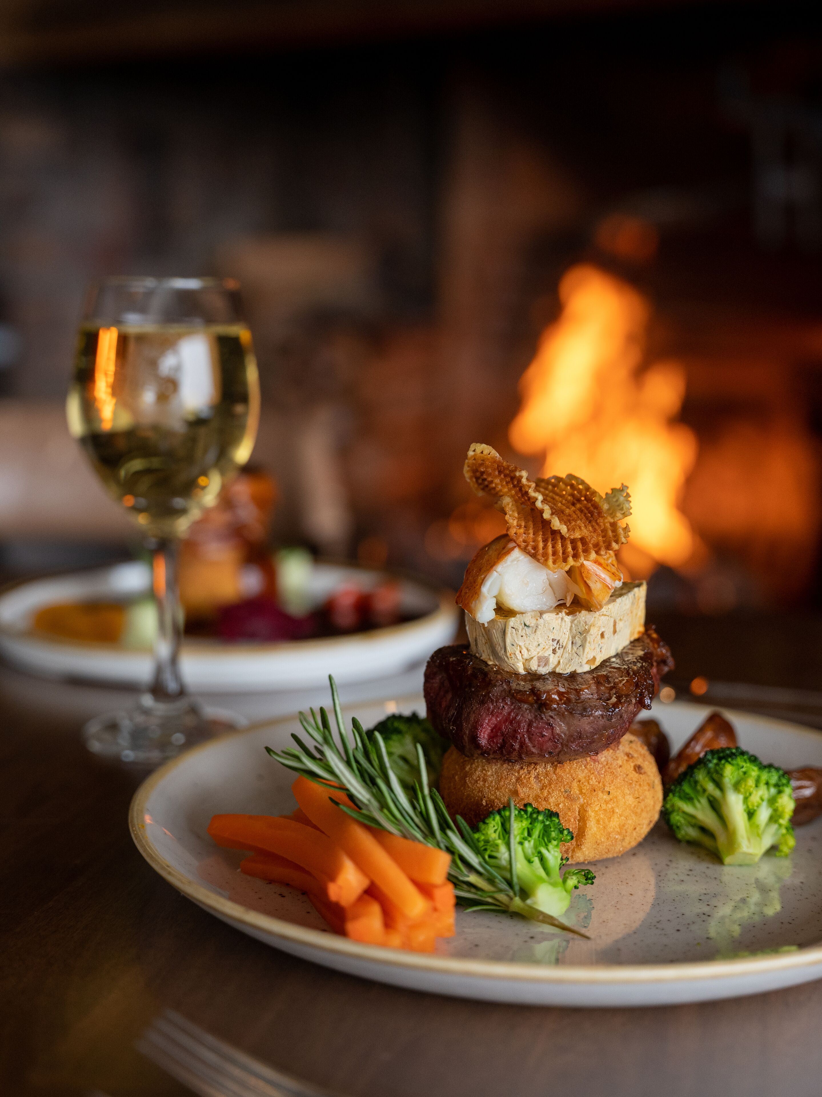 A plate with a burger, vegetables, and a glass of white wine.