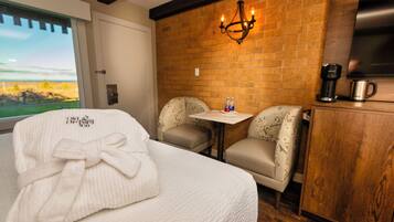 A hotel room with a bed, a table, two chairs, a coffee maker, and a TV on a wooden cabinet.