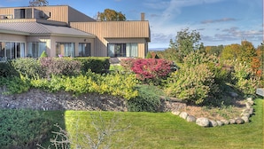 A modern house with a stone retaining wall, a well-maintained garden, and a clear sky.
