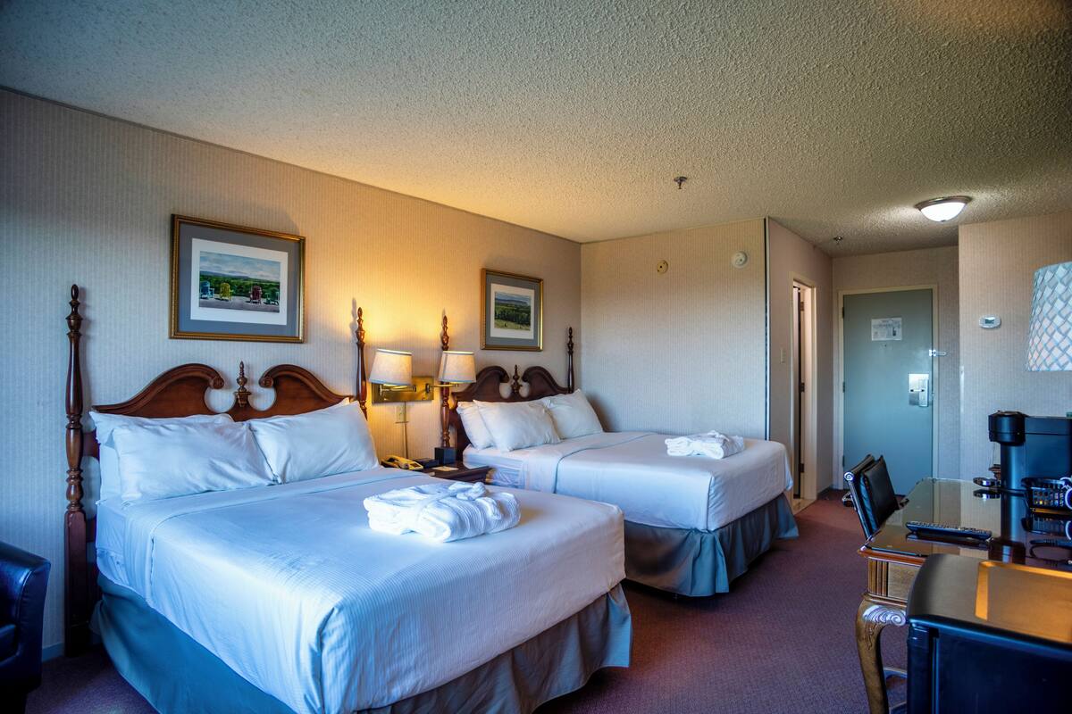 Habitación de hotel con dos camas, un escritorio y una silla. Se observan cuadros enmarcados en la pared y una puerta a la derecha.