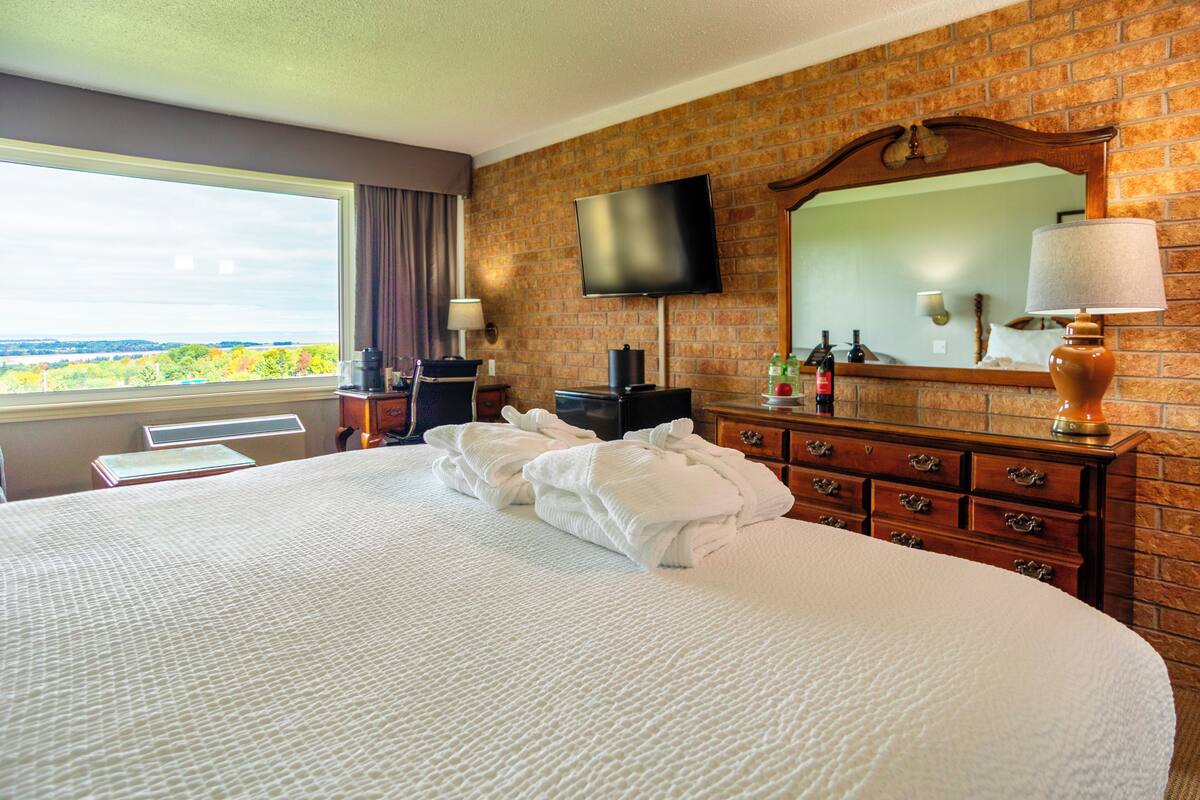 Habitación de hotel con una cama grande, televisión de pantalla plana, pared de ladrillo, ventana con vistas y cómoda con espejo.